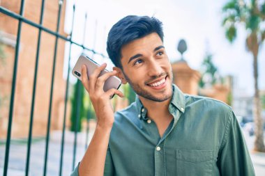 Genç Latin adam gülümsüyor. Şehirde akıllı telefon kullanarak mutlu bir sesli mesaj dinliyor..