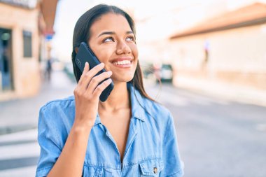 Genç Latin kız gülümsüyor. Şehirdeki akıllı telefondan konuşuyor..