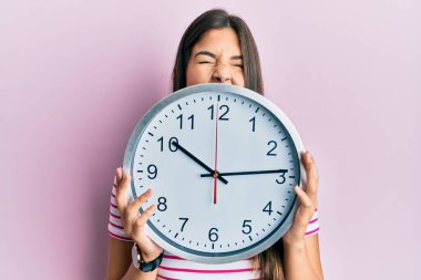 Genç esmer kadın elinde koca bir saat, yüzünü kapatıyor kızgın ve deli gibi bağırıyor sinirlenmiş ve öfkeli, öfkeyle bağırıyor.. 