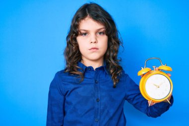 Uzun saçlı tatlı İspanyol çocuk çalar saat tutuyor. Duruşunu düşünüyor ve kendine güveniyor gibi görünüyor. 