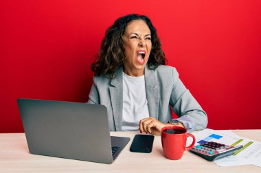 Ofiste çalışan güzel, orta yaşlı bir kadın kızgın ve kızgın bir şekilde bağıran, öfkeyle bağıran bir fincan kahve içiyor. öfke ve agresif konsept. 