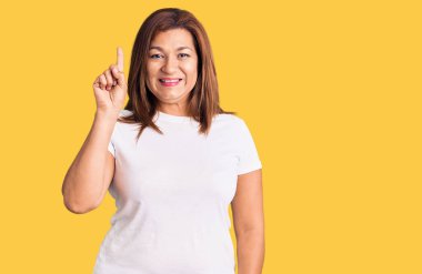 Güzel, orta yaşlı bir kadın izole edilmiş arka planda gülümsüyor ve kameraya bakıp zafer işareti yapıyor. İki numara..