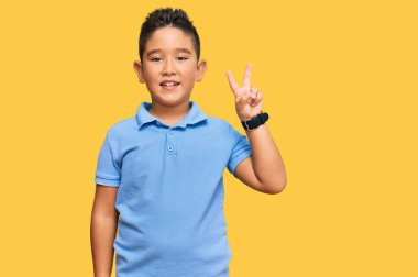 Küçük İspanyol çocuk gündelik kıyafetler giyip iki numarayı gösterip işaret ederken kendinden emin ve mutlu bir şekilde gülümsüyor.. 