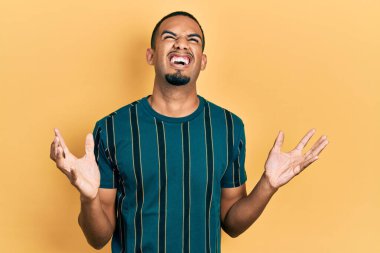 Genç, Afro-Amerikalı, günlük kıyafetler giymiş çılgın ve kızgın bir şekilde bağırıyor, agresif bir ifade ve kollarla bağırıyor. hüsran kavramı. 