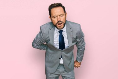 Orta yaşlı bir adam iş kıyafetleri giyiyor sırt ağrısı çekiyor, elleriyle dokunuyor, kas ağrısı çekiyor. 