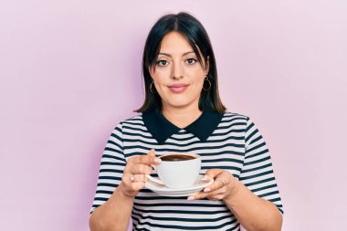 Bir fincan kahve içen genç İspanyol kadın yüzünde ciddi bir ifadeyle rahatlamış. Basit ve doğal bir şekilde kameraya bakıyorsun.. 