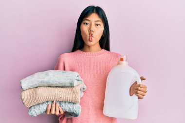 Genç Çinli kadın elinde deterjan şişesi ve kıyafetlerle balık suratlı ve şaşı gözlü çılgın ve komik.. 