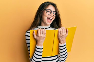 Genç beyaz kadın kitap okuyor, gözlük takıyor, gülüyor ve kahkahalar atıyor.. 