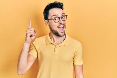 Gündelik kıyafetler giyen ve gözlüklü genç İspanyol başarılı bir fikirle işaret ediyor. Heyecanlı ve mutlu. Bir numara.. 