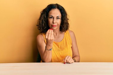 Güzel orta yaşlı kadın, gündelik giysiler içinde masaya oturmuş İtalyan jestleri yapıyor ve parmakları kendinden emin bir ifadeyle. 