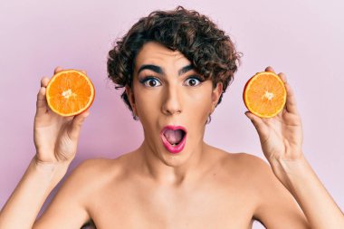 Genç adam elinde taze portakalla makyaj yapıyor. Şaşırmış ve şaşırmış bir ifade, korku ve heyecanlı bir yüz ifadesi var.. 