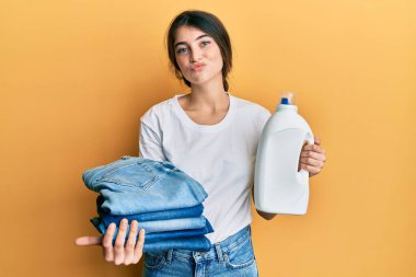 Çamaşır yıkayan, çamaşır deterjanı şişesi tutan, katlanmış kot pantolon giyen, kameraya bakıp öpüşen beyaz bir kadın. Güzel ve seksi. aşk ifadesi. 