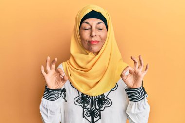 Orta yaşlı İspanyol kadın geleneksel İslami başörtüsü takıyor rahatla ve gözleri kapalı gülümse parmaklarıyla meditasyon hareketi yapıyor. yoga konsepti. 