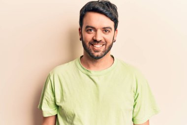 Yüzünde mutlu ve havalı bir gülümseme olan sıradan kıyafetler giyen genç İspanyol bir adam. şanslı kişi. 