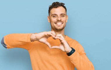 Gündelik kıyafetler giyen, aşık gülümseyen, elleriyle kalp sembolü yapan genç bir İspanyol. romantik kavram. 