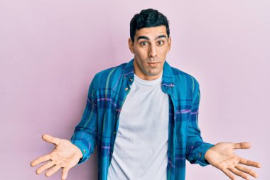 Sıradan kıyafetler giyen yakışıklı İspanyol bir adam. Kolları ve elleri havada, kafası karışmış bir ifade. şüphe kavramı. 