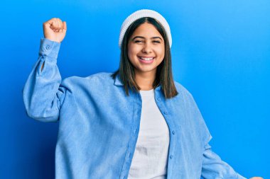 Şirin yün şapkalı genç Latin kadın mutlu ve neşeli dans ediyor, gülümsüyor rahat ve kendinden emin bir şekilde müzik dinliyor. 