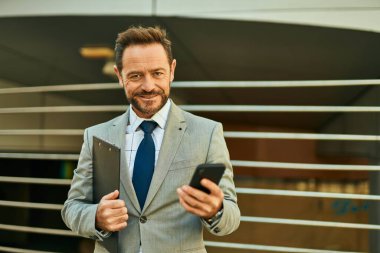 Şehirdeki akıllı telefondan gülümseyen orta yaşlı bir işadamı..