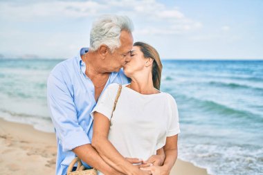 Orta yaşlı İspanyol çift mutlu bir şekilde gülüyor ve kumsalda yürüyorlar.