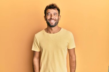 Sakallı, sarı tişörtlü, mutlu ve havalı bir gülüşü olan yakışıklı bir adam. şanslı kişi. 