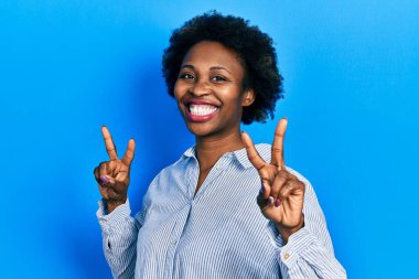 Gündelik giysiler giymiş genç Afro-Amerikan kadın kameraya bakıp zafer işareti yapıyor. İki numara.. 