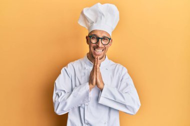 Kel, sakallı, profesyonel aşçı üniforması giyen, elleriyle dua eden, affedilmek isteyen, kendinden emin, gülümseyen bir adam.. 