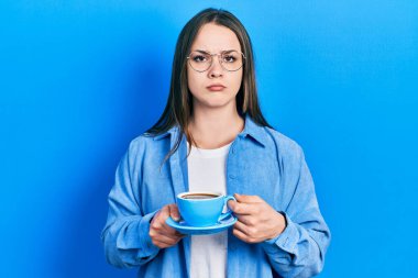 Latin kökenli genç bir kız bir fincan kahve içiyor şüpheci ve gergin, sorun yüzünden surat asıyor. negatif kişi. 