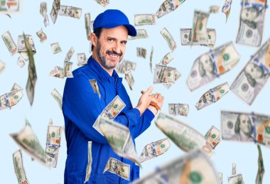 Orta yaşlı, yakışıklı, tamirci üniforması giyen ve gülümseyerek içeri girmeye davet eden bir adam.