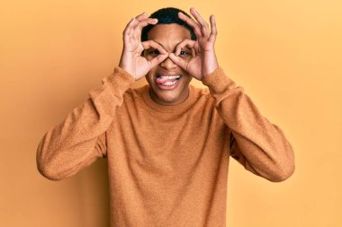 Genç, yakışıklı İspanyol bir adam sıradan bir kazak giyiyor. Dürbün gibi jest yapıyor. Dürbün dilini çıkarıyor, gözler parmaklarından bakıyor. çılgın ifade. 