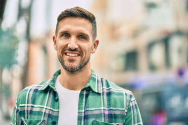 Genç beyaz adam gülümseyerek şehirde mutlu mesut duruyor..