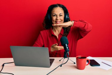 Güzel, orta yaşlı bir kadın radyo stüdyosunda çalışıyor. Büyük ve büyük boy işareti gösteren el kol hareketleri yapıyor. Ölçü sembolü. Kameraya bakıp gülümsüyor. ölçüm kavramı. 