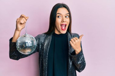 Parlak disko topunu tutan genç İspanyol kız başparmağıyla yan tarafa doğru işaret ediyor mutlu bir şekilde gülümsüyor. 