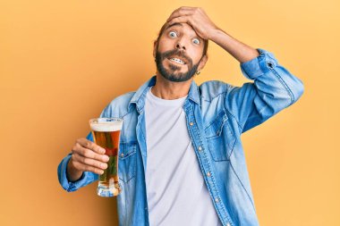 Uzun saçlı ve sakallı çekici bir adam yarım litre bira içiyor. Stresli ve hayal kırıklığına uğramış, şaşırmış ve kızgın bir yüzü var. 