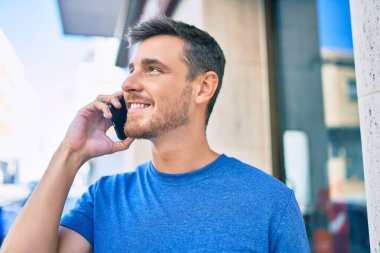 Genç beyaz adam gülümsüyor. Şehirdeki akıllı telefondan konuşuyor..