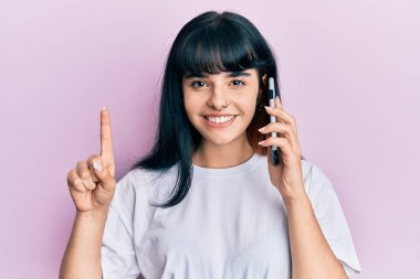 Genç İspanyol kız akıllı telefonda konuşuyor bir fikirle gülümsüyor ya da soru işareti yapıyor mutlu bir yüzle, bir numara 