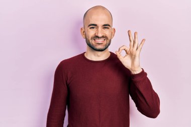 Gündelik kıyafetler giyen genç kel adam olumlu gülümsüyor. El ve parmaklarıyla 