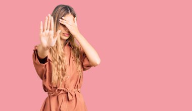 Yazlık tulum giyen, gözleri ellerle kaplayan, üzgün ve korku ifadeleriyle jest yapan güzel, beyaz bir kadın. utangaç ve olumsuz kavram. 