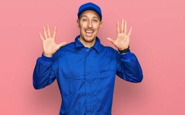 Sakallı, inşaatçı tulumu giyen kel bir adam on numaralı parmaklarıyla onu gösterirken kendinden emin ve mutlu bir şekilde gülümsüyor.. 