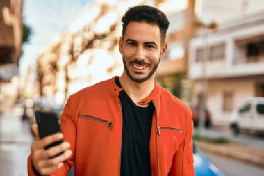 Genç İspanyol adam şehirde akıllı telefon kullanarak mutlu gülümsüyor..