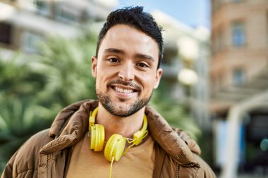 Şehirde kulaklık takarak mutlu gülümseyen genç İspanyol adam..