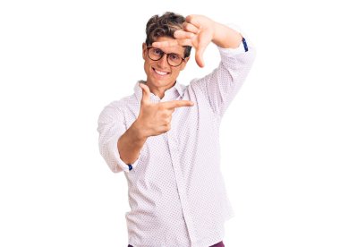 İş kıyafetleri ve gözlük takan genç yakışıklı adam gülümsüyor. Elleriyle ve parmaklarıyla gülüyor. yaratıcılık ve fotoğrafçılık kavramı. 