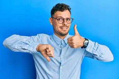 Gündelik kıyafetler giyen ve gözlük takan genç İspanyol bir adam başparmak kaldırıyor, anlaşmazlık ve anlaşma ifadesi. çılgın çatışma 