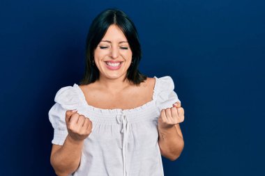 Gündelik kıyafetler giyen genç İspanyol kadın başarı için heyecanlı kolları havada ve gözleri kapalı zaferi kutlarken gülümsüyor. Kazanan konsept. 