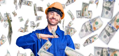 İşçi üniforması giyen genç İspanyol adam. Elleriyle işaret ediyor. Büyük ve büyük boy işareti, ölçü işareti. Kameraya bakıp gülümsüyor. ölçüm kavramı.