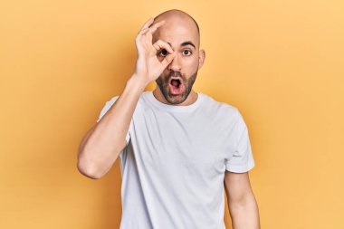 Sıradan beyaz tişört giyen genç kel adam şaşırmış yüz ifadesiyle şok olmuş, parmaklarından bakan gözler. İnançsız ifade. 