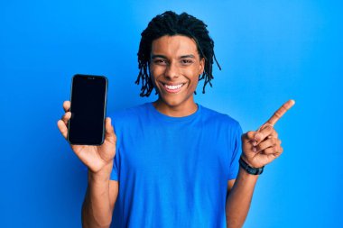 Genç Afro-Amerikan adam elinde akıllı telefonuyla boş ekranda gülümsüyor. 