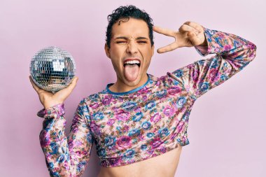 Yakışıklı adam makyaj yapıp parlak disko topunu tutuyor. Dilini dışarı çıkarıyor. Komik bir ifadeyle.. 