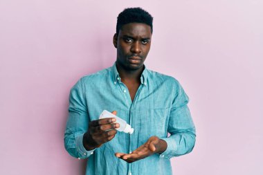 El dezenfektanı jeli kullanan yakışıklı siyahi adam depresif ve endişeli, sinirli ve korkmuş. hüzünlü ifade. 