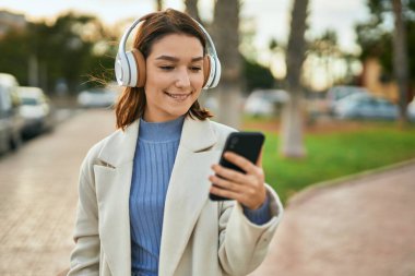 Genç İspanyol kadın şehirde akıllı telefon ve kulaklık kullanarak mutlu bir şekilde gülümsüyor..