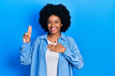 Genç Afro-Amerikalı kadın, günlük kıyafetler giymiş, gülümsüyor, elleri göğsünde ve parmakları havada küfür ediyor, sadakat yemini ediyor. 